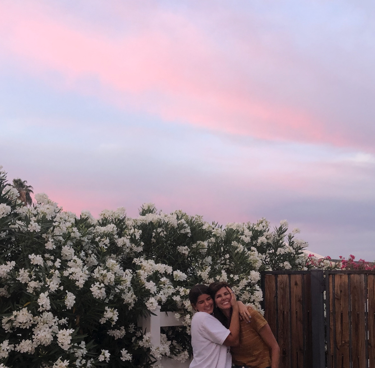 Grace hugging Shawni under a pink sunset sky